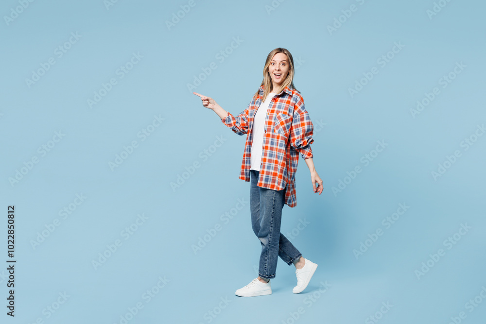 Full body side profile view young smiling happy woman wears red shirt t-shirt casual clothes walk go point finger aside isolated on plain pastel light blue cyan background studio. Lifestyle concept. Full body side profile view young smiling happy woman wears red shirt t-shirt casual clothes walk go point finger aside isolated on plain pastel light blue cyan background studio. Lifestyle concept.