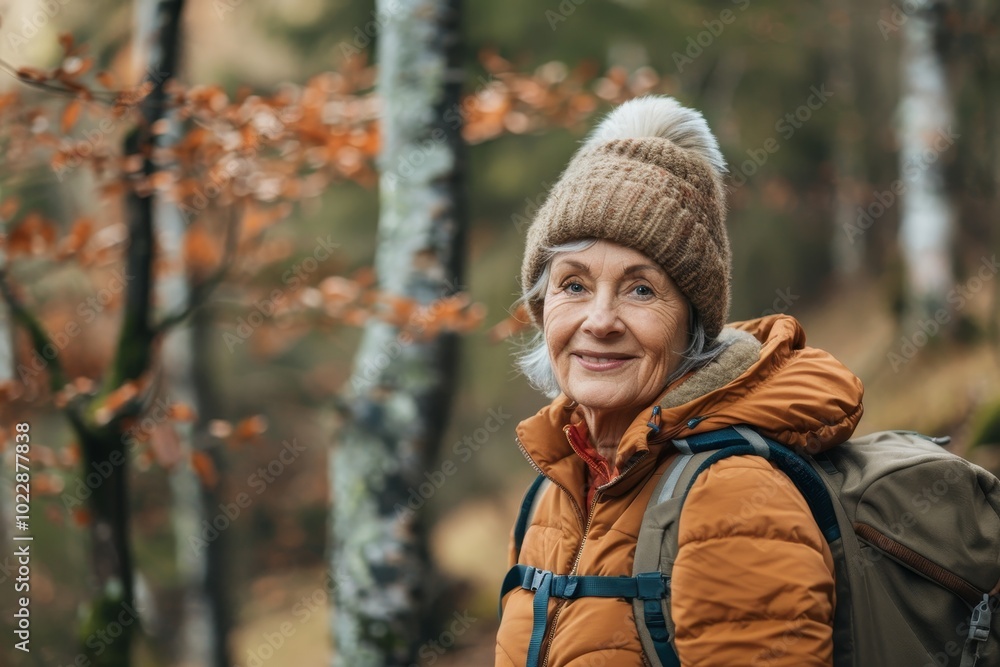 An older woman smiles warmly while hiking through a vibrant forest filled with autumn leaves. She is dressed warmly and carries a backpack, embracing the tranquility of nature. An older woman smiles warmly while hiking through a vibrant forest filled with autumn leaves. She is dressed warmly and carries a backpack, embracing the tranquility of nature.