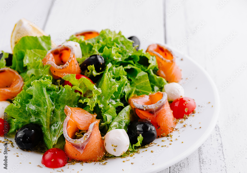 Delicious salad with smoked salmon, mozzarella and cherry tomatoes on white table Delicious salad with smoked salmon, mozzarella and cherry tomatoes on white table