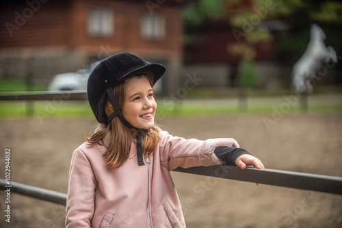 Little girl in a helmet stands on a ranch, learning to ride horses. Portrait of a child girl in jockey a horse, horse riding training. Little girl a jockey helmet smiling in the at riding stable photo