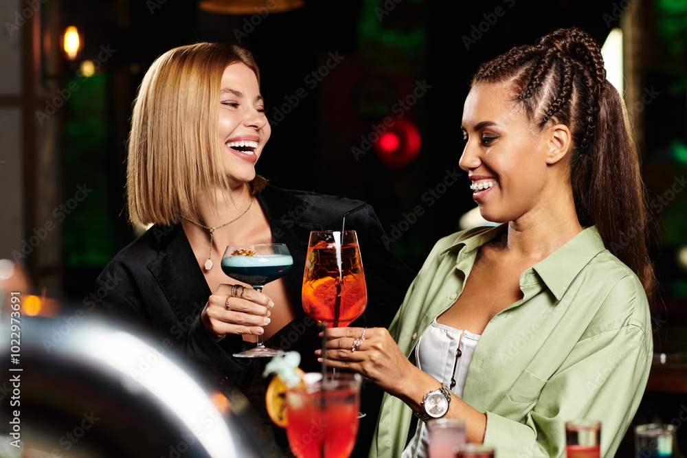 Two young professionals share a moment of joy while toasting with colorful cocktails at a party. Two young professionals share a moment of joy while toasting with colorful cocktails at a party.