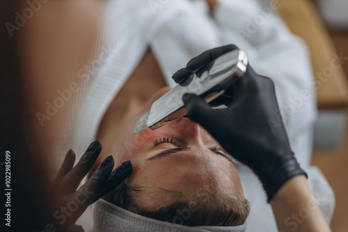 Cosmetologist making facial treatment with ultrasonic spatula to young woman.