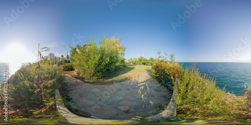 A peaceful coastal garden with lush greenery overlooking the ocean, captured in a 360-degree panorama. The bright sunlight and clear blue sky enhance the serene and natural beauty of the scene.