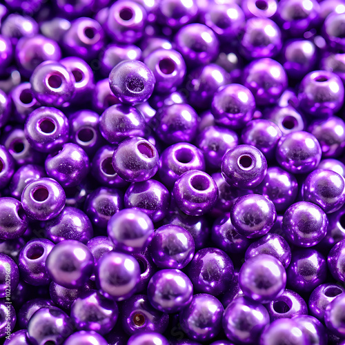 A close-up of shiny purple beads fills the frame, with their metallic and reflective surfaces catching the light, creating a striking and vibrant image.