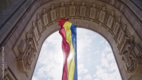 The Romanian flag waving in the wind at the triumphal arch. The Red, Yellow and Blue tricolor. The wind that flutters and moves the flag hanging from the monument of the triumphal arch in Bucharest.