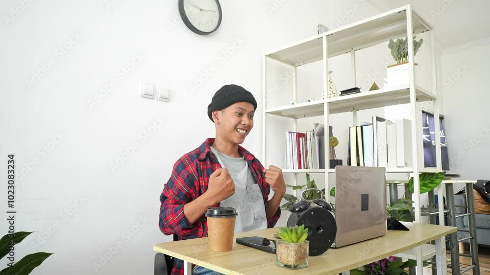 Young Asian Male Entrepreneur Sitting At Desk Looking At Laptop Screen, Raising Hands With Excitement Celebrating Success Selling Young Asian Male Entrepreneur Sitting At Desk Looking At Laptop Screen, Raising Hands With Excitement Celebrating Success Selling