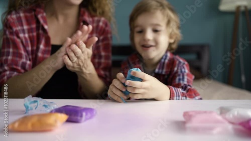 Child boy with his mother sculpting from play clay sitting on bed in the room