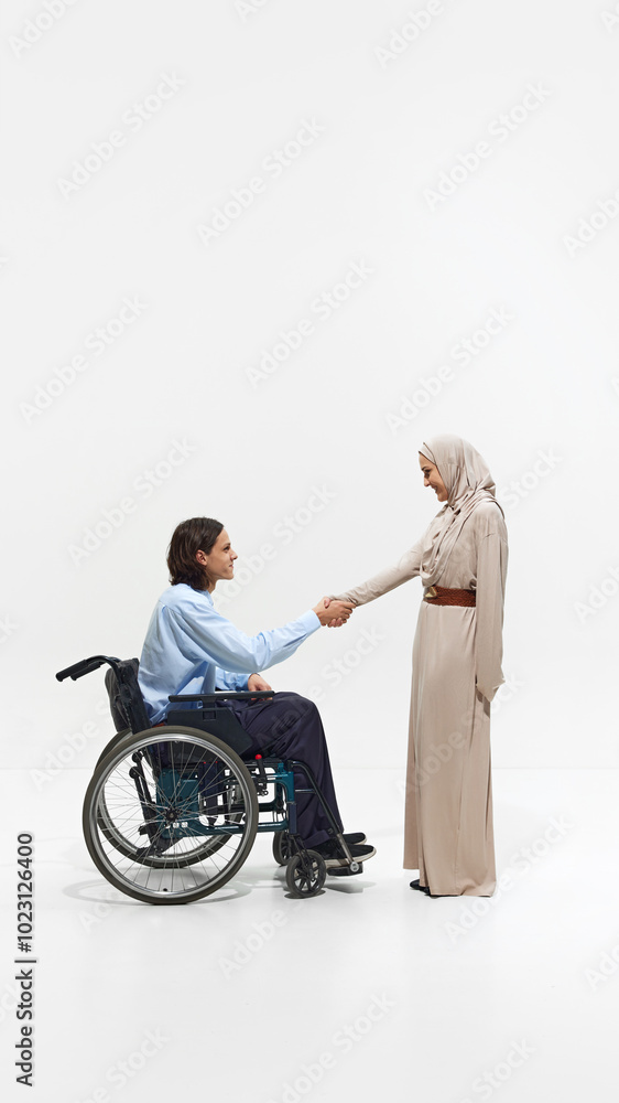 Man in wheelchair shaking hands with Muslim woman in beige dress, showcasing mutual respect and inclusion in professional setting. Concept of business, dei, equality, support Man in wheelchair shaking hands with Muslim woman in beige dress, showcasing mutual respect and inclusion in professional setting. Concept of business, dei, equality, support