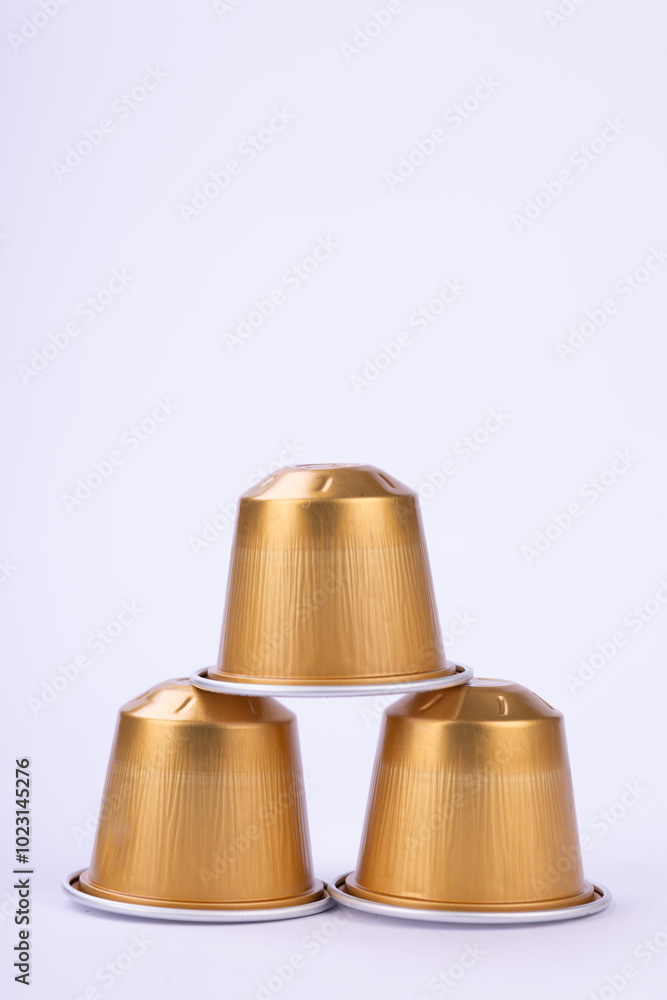 Golden Coffee Capsules Arranged in Pyramid Shape on White Background Golden Coffee Capsules Arranged in Pyramid Shape on White Background