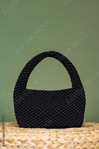 Knitted black handamde bag on the straw podium. Yarn crocheted female bag. Sustainable shopping. Eco friendly concept. photo