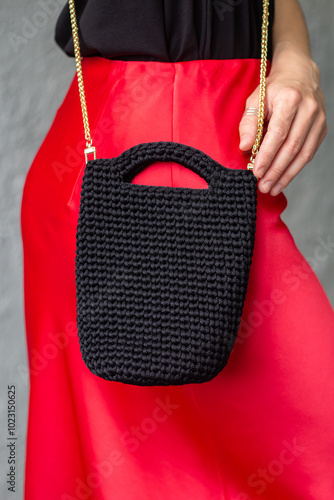 Woman holds yarn knitted handmade black bag in her hand. Female with cross-body bag on walk. Sustainable shopping. Eco freiendly photo