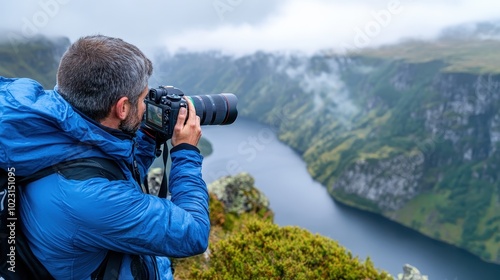 A photographer in a blue jacket captures a breathtaking river canyon view surrounded by misty mountains, showcasing nature's beauty and the art of photography.