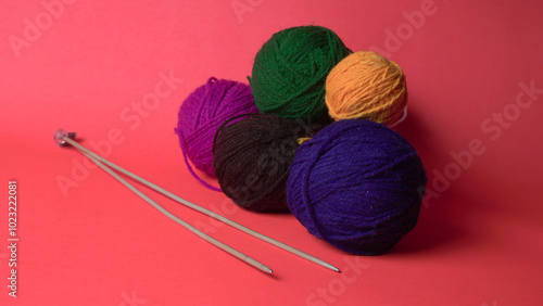 A Piece of knitting with color threads ball of yarn and a knitting needle on red background.