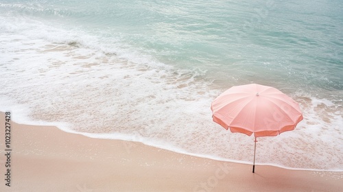 A pink beach umbrella standing alone on the sandy shore, with the gentle waves of the ocean in the background.