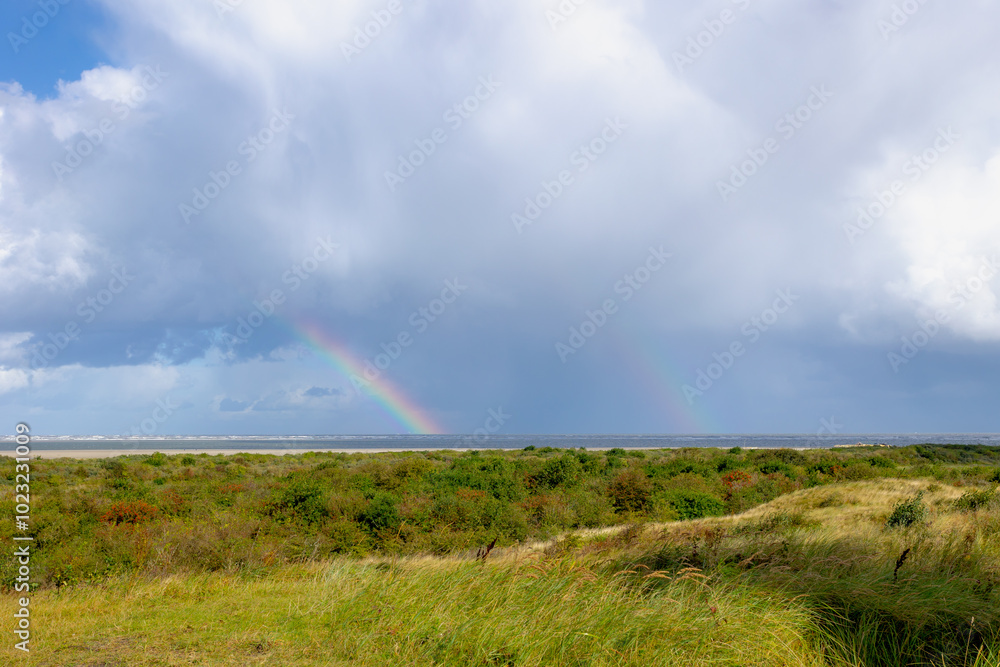 Dune with european marram grass, White sand beach with blue sky and rainbow on the sea, Schiermonnikoog is a municipality and national park in the Northern Netherlands, One of the West Frisian Islands Dune with european marram grass, White sand beach with blue sky and rainbow on the sea, Schiermonnikoog is a municipality and national park in the Northern Netherlands, One of the West Frisian Islands