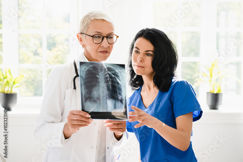 Two female doctors nurses interns caregivers checking discussing diagnosis on x-ray photo of lungs of patient at hospital photo