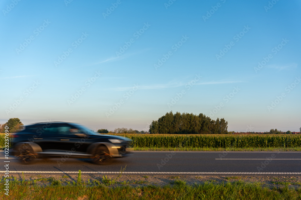 Blurred black car driving on a paved road on a sunny day. Concept of rapid transportation, road safety and rural landscape. High quality photo Blurred black car driving on a paved road on a sunny day. Concept of rapid transportation, road safety and rural landscape. High quality photo