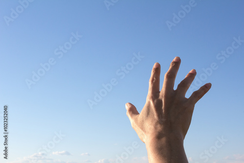 A shadowy male hand reaches out against the blue sky.