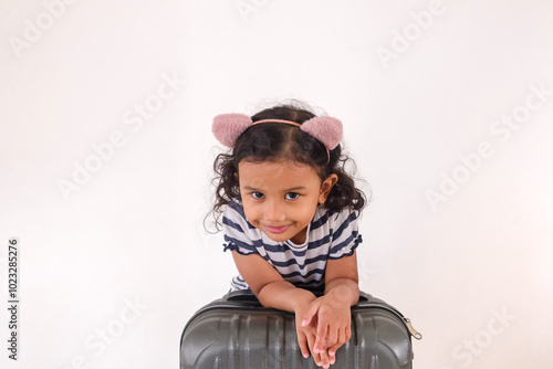 A cheerful little Asian girl posing with a suitcase on a white background