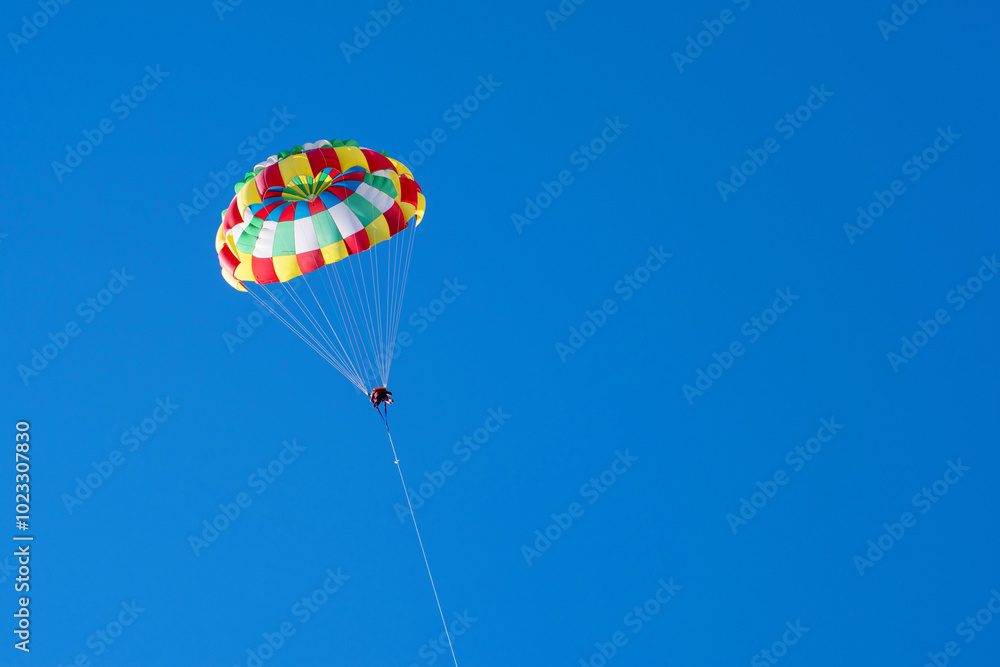 Tourists fly on a bright paraglider against the blue sky in the summer on a sunny day. Beach holidays, tourist marine entertainment. Parasailing Tourists fly on a bright paraglider against the blue sky in the summer on a sunny day. Beach holidays, tourist marine entertainment. Parasailing
