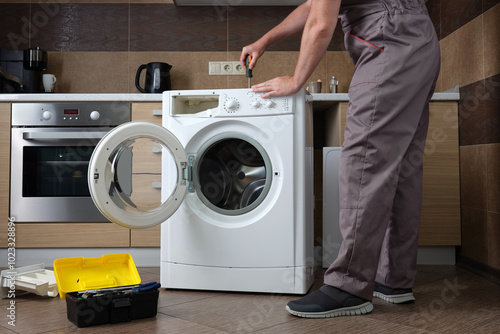 A adult household appliance repairman disassembling a washing machine with a screwdriver. photo