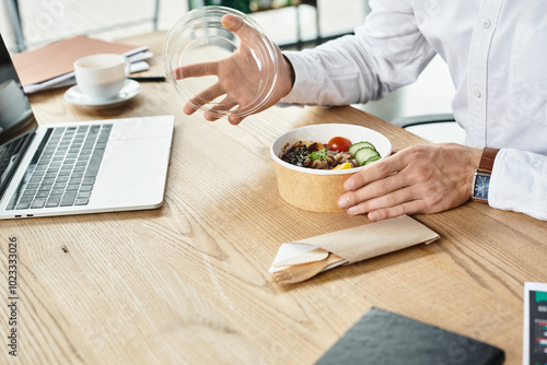 A dedicated businessman in a white shirt takes a lunch break, savoring a healthy meal while working.