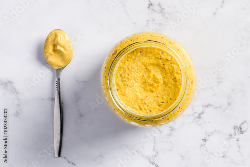 Top view of a spoon and open jar full with musterd on a marble background.