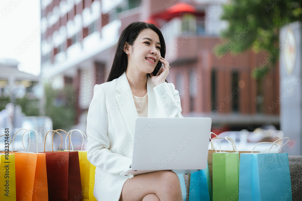 Fototapeta premium Asian woman smiles happily. She enjoys the city life and the excitement of successful shopping amidst modern buildings and bustling retail stores.