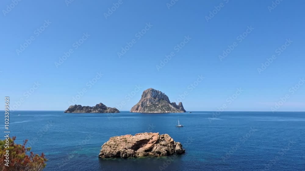 Boat sails across the calm waters of the Mediterranean Sea near the iconic Es Vedra island, located off the coast of Ibiza on a clear summer day Boat sails across the calm waters of the Mediterranean Sea near the iconic Es Vedra island, located off the coast of Ibiza on a clear summer day