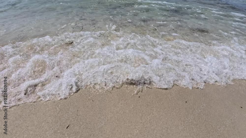 Video shows a wider shot of small waves gently washing over wet sand as clear water ripples across the shoreline creating a calm beach scene Video shows a wider shot of small waves gently washing over wet sand as clear water ripples across the shoreline creating a calm beach scene