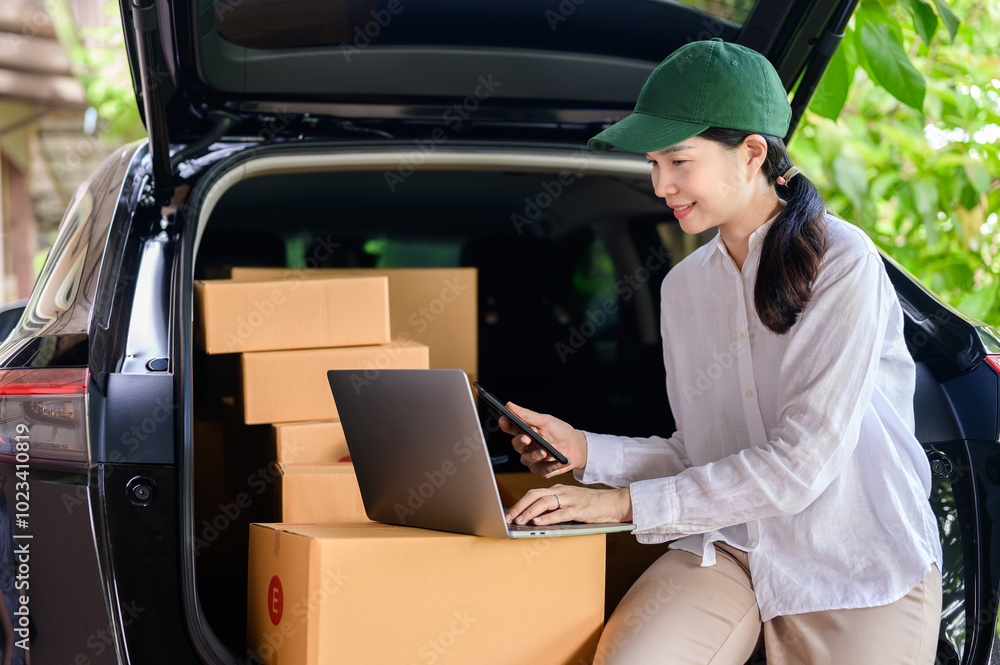 An Asian woman who works as an online seller is near the back of a truck, delivering a package while using a laptop. An Asian woman who works as an online seller is near the back of a truck, delivering a package while using a laptop.