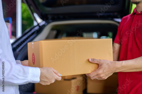 Canvas Print A close-up of a parcel box as a male delivery man holding a parcel box is delivering a parcel to a satisfied female customer and friendly staff at the customer's home