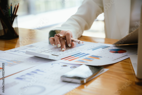 A focused businesswoman uses a laptop and a calculating machine at her desk to analyze financial documents. She examines charts and reports, managing budgets and expenses for effective corporate accou photo