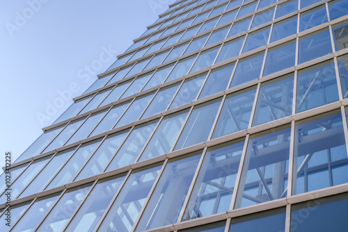 A modern glass building rises into the sky, showcasing its grid-like facade and reflecting the clear blue atmosphere. The architectural lines create a sense of depth and symmetry.