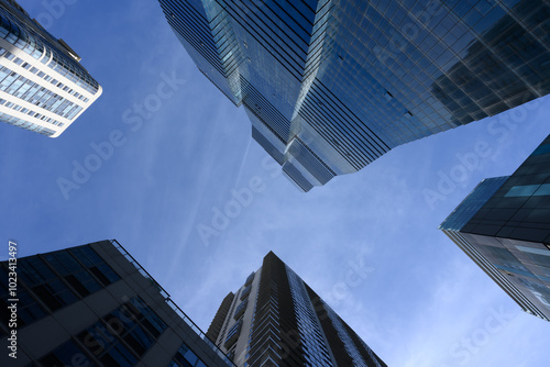 Skyscrapers tower above, converging towards a bright blue sky, creating a dramatic and imposing perspective. 