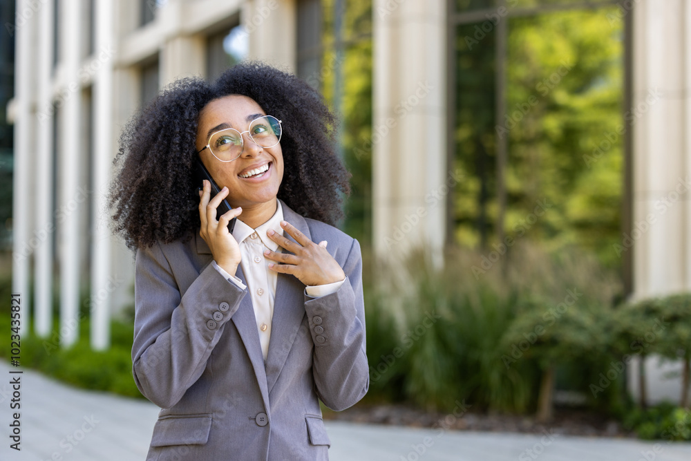 African american business woman happily talking on phone, standing in front of office building. Confident expression and stylish attire reflect professional success and joyful communication. African american business woman happily talking on phone, standing in front of office building. Confident expression and stylish attire reflect professional success and joyful communication.
