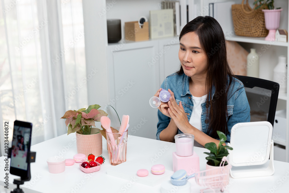 Young beautiful Asian girl reviewing moisturizing body lotion cream product to make glow skin testing on arm on social media online live recording smartphone with bestseller at modern room. Stratagem. Young beautiful Asian girl reviewing moisturizing body lotion cream product to make glow skin testing on arm on social media online live recording smartphone with bestseller at modern room. Stratagem.