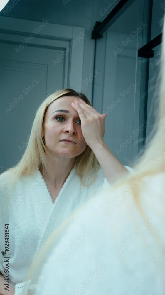Woman at home in the bathroom against the mirror in a bathrobe performs a home facial skin care routine, applying moisturizer to her facial skin Woman at home in the bathroom against the mirror in a bathrobe performs a home facial skin care routine, applying moisturizer to her facial skin