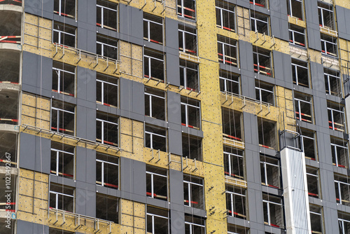 Workers are actively installing windows and cladding on a high-rise building under construction in a bustling city during the day photo