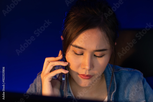 Young beautiful Asian creative woman calling on phone to customer or coworker informing strategy marketing creator plan while searching market analysis on pc at neon modern office at night. Stratagem.