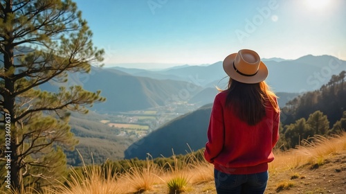 A woman wearing a vibrant red sweater and hat stands on a hilltop overlooking a breathtaking valley framed by majestic mountains. photo