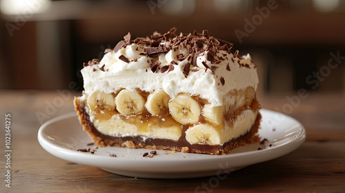 Wallpaper Mural A slice of Banoffee pie on a white plate, with layers of bananas, toffee, and whipped cream, topped with chocolate shavings, on a rustic wooden table. Torontodigital.ca