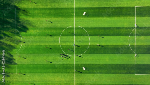 Aerial view of a soccer field with players and shadows. An aerial view of a soccer field with vivid green grass and a clearly marked center circle. photo