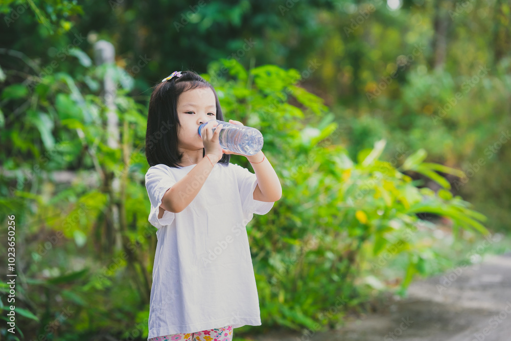 A thirsty girl is drinking water from a plastic bottle because of the hot weather. Copy Space. A thirsty girl is drinking water from a plastic bottle because of the hot weather. Copy Space.