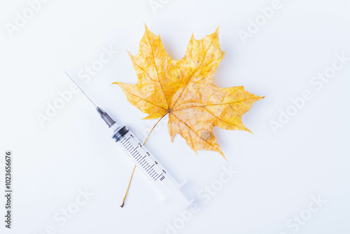 Autumn maple leaf and syringe with vaccine on white background. Vaccination against colds.