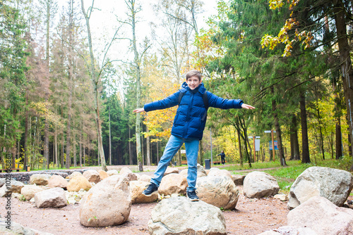 A 12 year old boy stands on a large rock in an autumn park. The teenager walks near a cascade of ponds in Borovsky Park in Moscow. photo