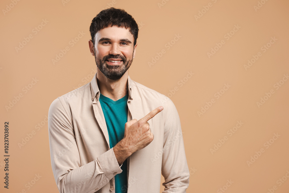 Happy bearded Hispanic man wearing stylish shirt pointing finger on copy space on beige background Happy bearded Hispanic man wearing stylish shirt pointing finger on copy space on beige background