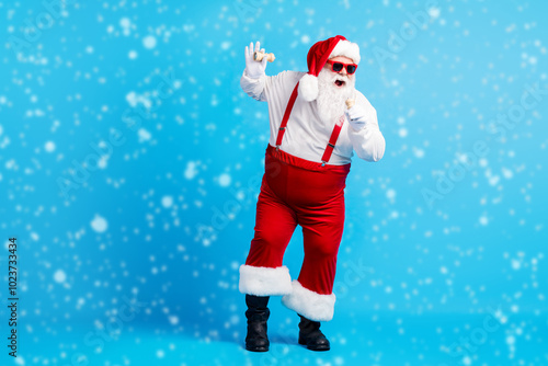 Full body photo of stylish crazy funky cool hipster santa claus with big abdomen sing x-mas christmas song pepper mic wear red suspenders overalls sunglass isolated blue color background