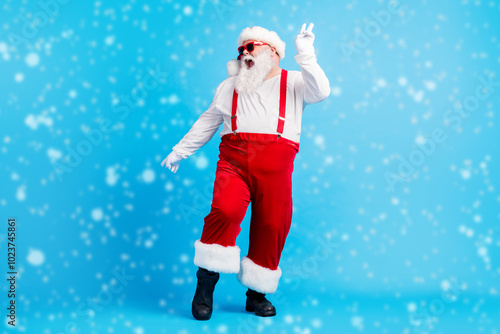 Full length photo of crazy funky santa claus with big stomach beard dance x-mas christmas discotheque wear suspenders overalls sunglass headwear isolated blue color background photo