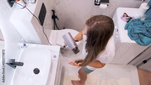 A young girl dries her hair with a hairdryer in the bathroom at home. Kazan, Russia - 13 Aug 2024
